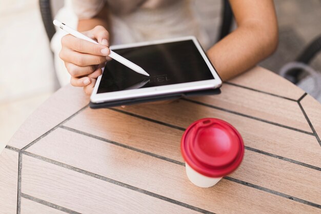Close-up of a girl using stylus on digital tablet with takeaway coffee cup on table