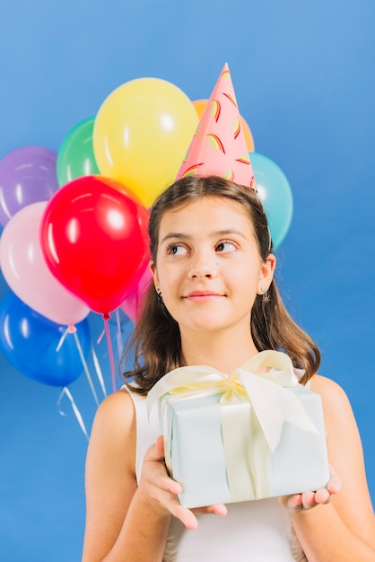 Close-up of a girl with birthday gift in front of colorful balloons