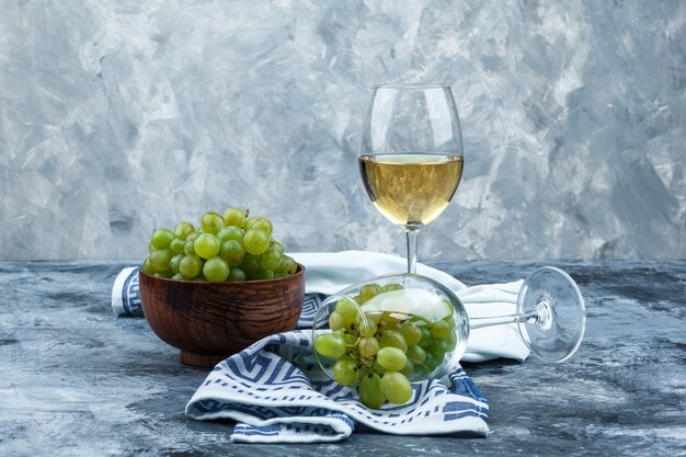 Close-up glass of white grapes with glass of whisky, bowl of grapes, kitchen towel on dark and light blue marble background. horizontal