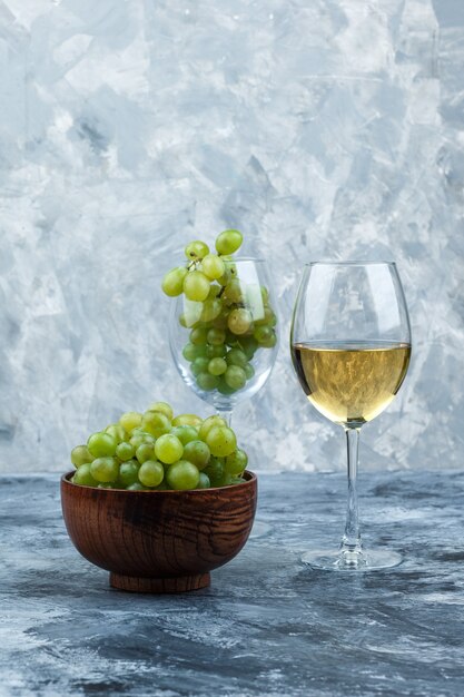 Макро стакан белого винограда со стаканом виски, миской винограда, кухонным полотенцем на темно-синем мраморном фоне. вертикальный