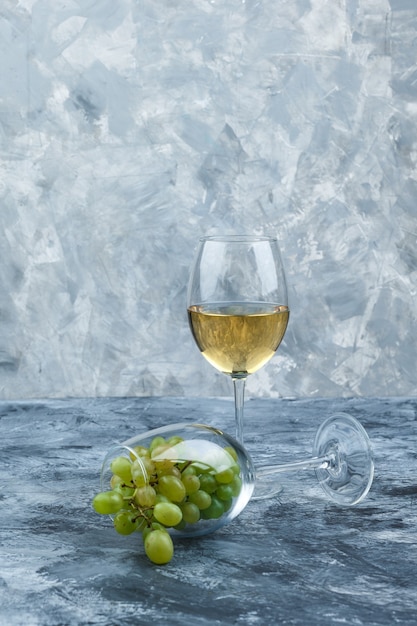 Free photo close-up glass of white grapes with glass of whisky on dark and light blue marble background. vertical