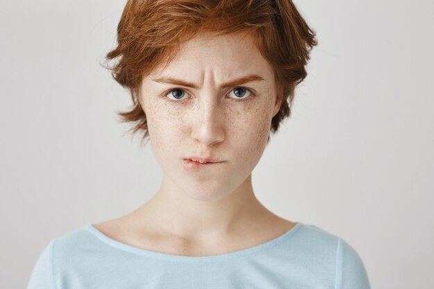 Close-up of gloomy redhead girl posing against the white wall