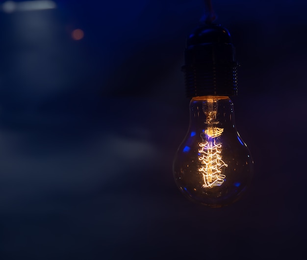 Close up of a glowing light bulb hanging in the dark copy space.