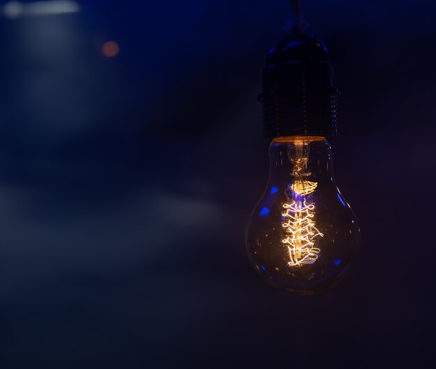 Close up of a glowing light bulb hanging in the dark copy space.