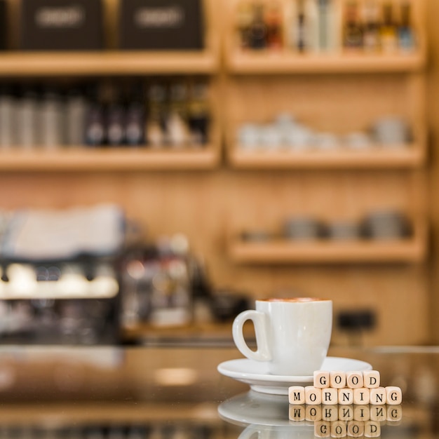 Free photo close-up of good morning wooden blocks with cup of coffee on glass cabinet