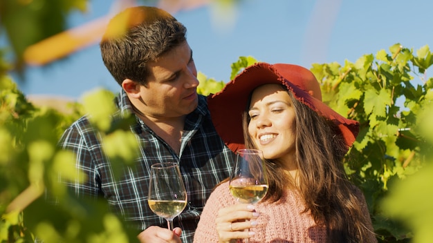 Close up of gorgeous couple embracing each other while holding glasses of wine in hands.