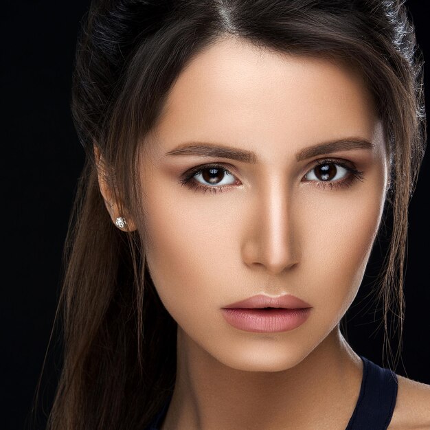 Close up of gorgeous and seductive woman with perfect bronze clean skin plumps lips confident looking at camera Young brunette girl after procedure and makeup in beauty salon Concept of beauty