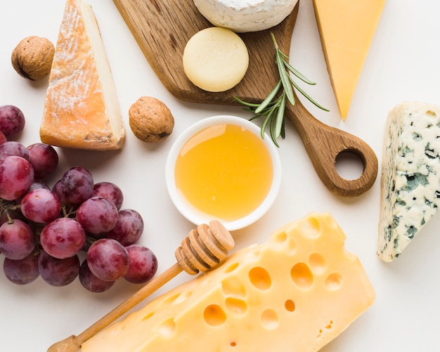 Close-up gourmet assortment of cheese on wooden cutting board honey and grapes