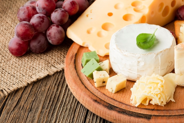 Close up gourmet cheese assortment on wooden cutting board with grapes