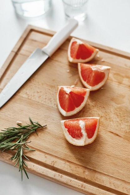 Close up of grapefruit pieces knife and rosemary on wooden desk. Copy space.