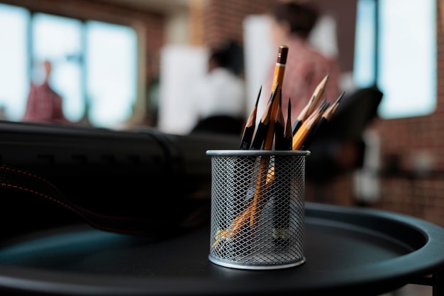 Close up of graphic pencils stand standing on table in creativity school studio. In background diverse team drawing vase sketch on canvas working at sketching technique. New years resolutions