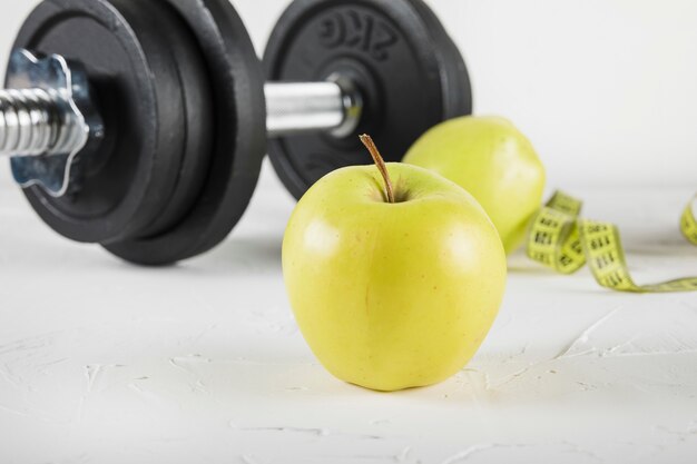 Close-up of green apple and dumbbell on white surface