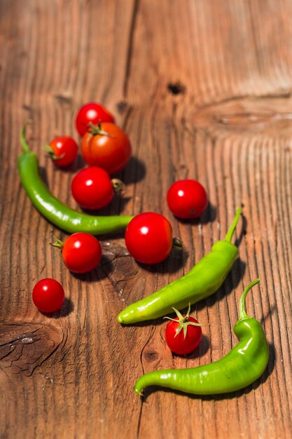 Close-up of green chili peppers and red cherry tomatoes on wooden backdrop