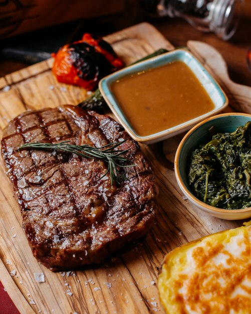 Close up of grilled beef steak with baked potato and sauce on a wooden board
