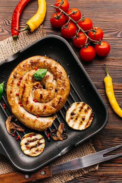 Close-up of grilled spiral sausages with vegetables and spices in pan