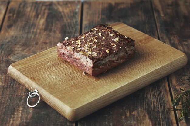 Close up grilled square meat with spices and salt isolated on wooden board on vintage table