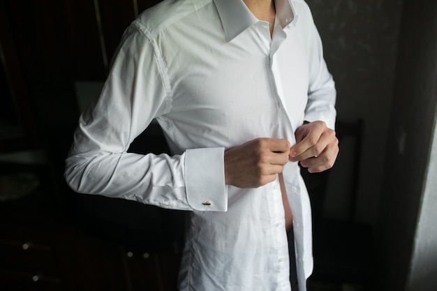 Close-up of groom buttoning his shirt