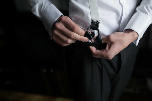 Close-up of groom placing suspenders