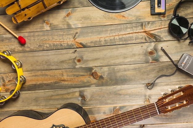 Close-up of guitar; headphone; tambourine; xylophone; headphone and radio on wooden table with space for text