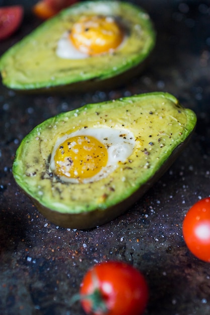 Close-up of halved avocado with egg yolk and tomatoes on kitchen worktop