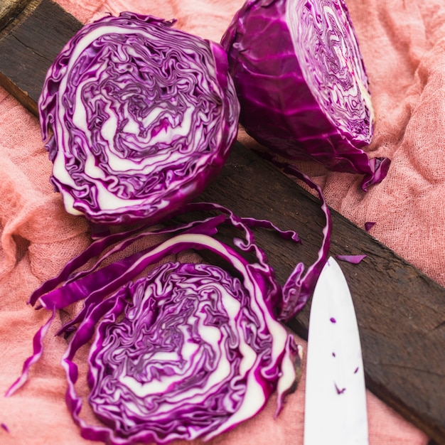 Close-up of halved fresh purple cabbage and knife on cloth