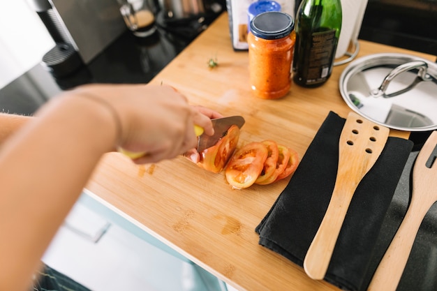 Close-up of hand cutting tomato slices with knife