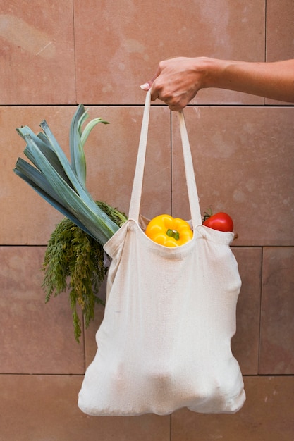 Закройте руку, держащую сумку с овощами