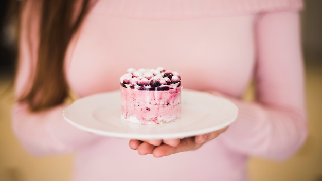 Close-up of hand holding blue berry cake on white plate