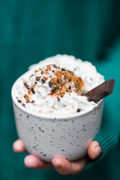 Close-up of hand holding cappuccino in a white cup with cream and chocolate