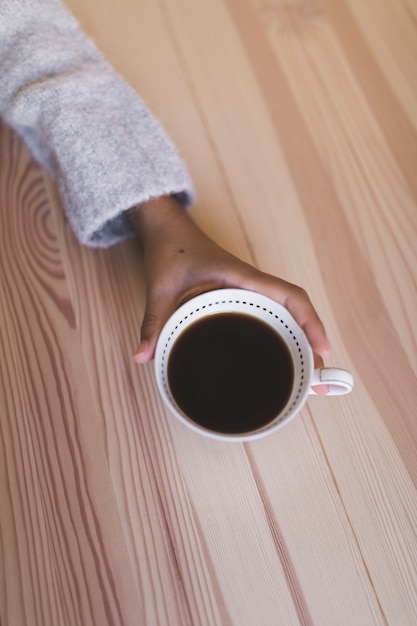 Close-up of hand holding cup of coffee over the wooden desk