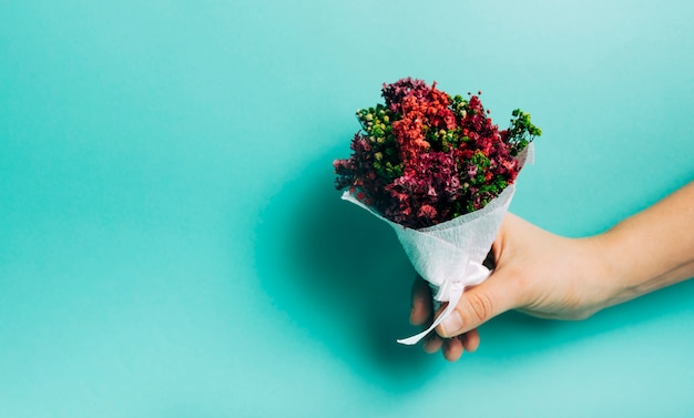 Free photo close-up of hand holding decorative flower bouquet against turquoise background