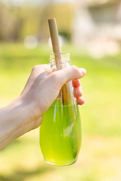 Close-up hand holding glass bottle with juice and paper straw