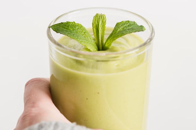 Close-up hand holding green smoothie and mint in glass