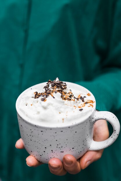 Close-up of hand holding hot chocolate cup with whipping cream and chocolate chips