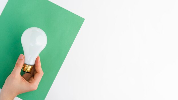 Крупный план руки, держащей лампочку над зеленой бумагой на белом фоне