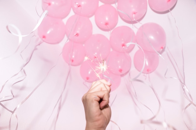 Close-up of hand holding lighted sparkler under the decorative ceiling with pink balloons