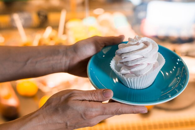 Close-up of hand holding meringue in cupcake wrapper on blue ceramic plate