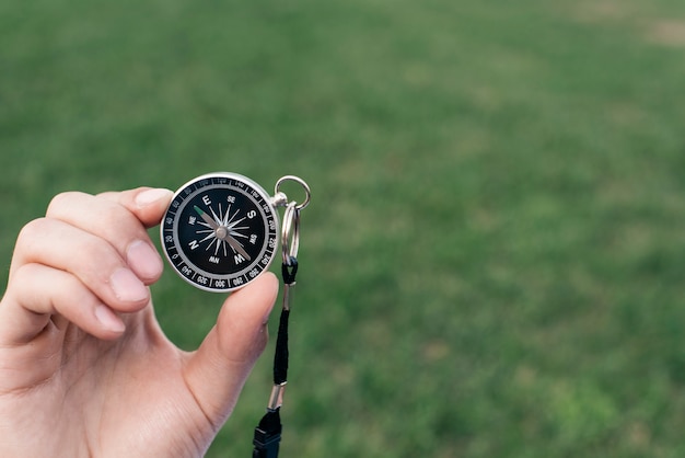 Close-up of hand holding navigational compass against green blurred background