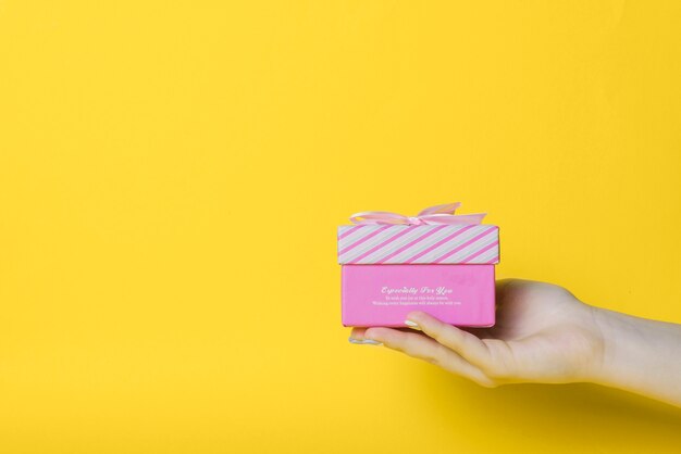 Close-up of hand holding pink box against yellow background