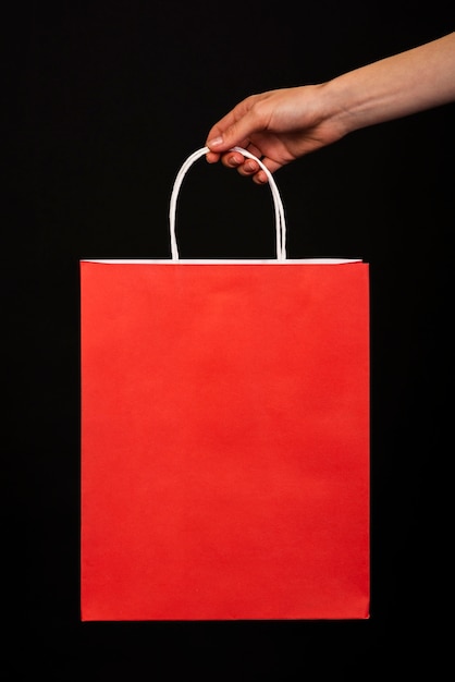 Close-up of a hand holding a red shopping bag on a black background 