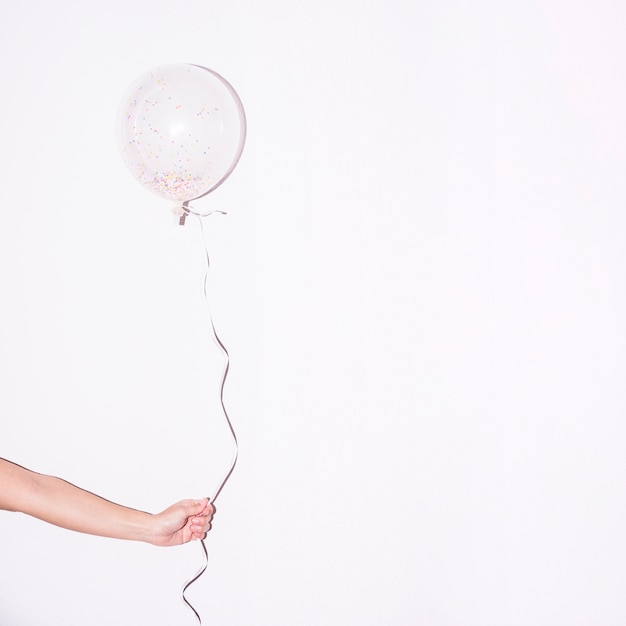 Close-up of hand holding single white balloon with colorful sprinkle inside it against white backdrop