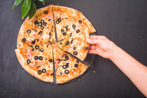 Close-up of hand holding slice of pizza on dark background