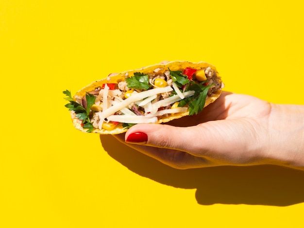 Close-up hand holding taco with yellow background