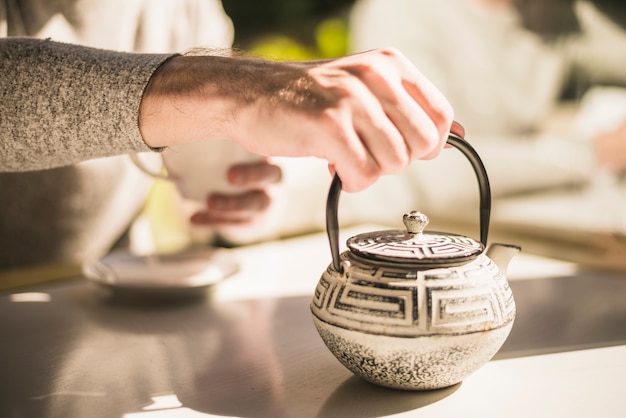 Close-up of hand holding traditional kettle on table