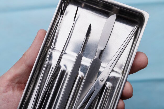 Close-up of hand holding tray with medical scalpel and tools