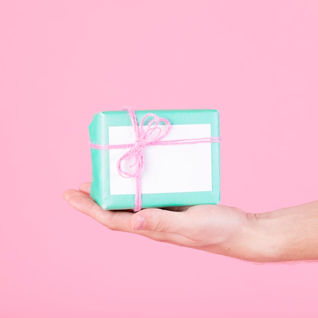 Close-up of a hand holding wrapped turquoise gift box against pink background