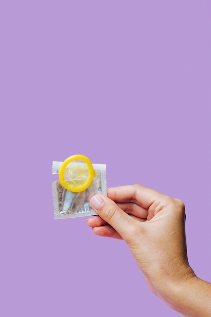 Close-up hand holding yellow condom 