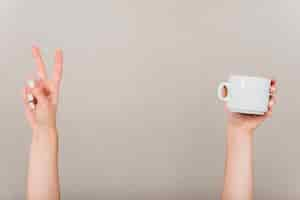 Free photo close-up of hand making peace gesture and white cup against colored backdrop