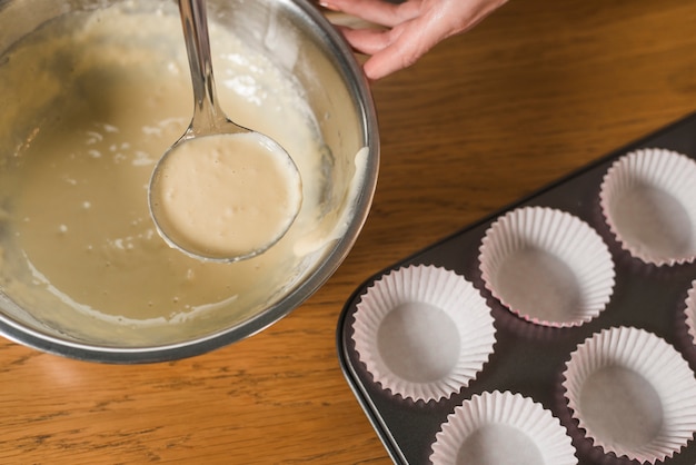 Close-up of hand pouring cake mix into baking muffins tray