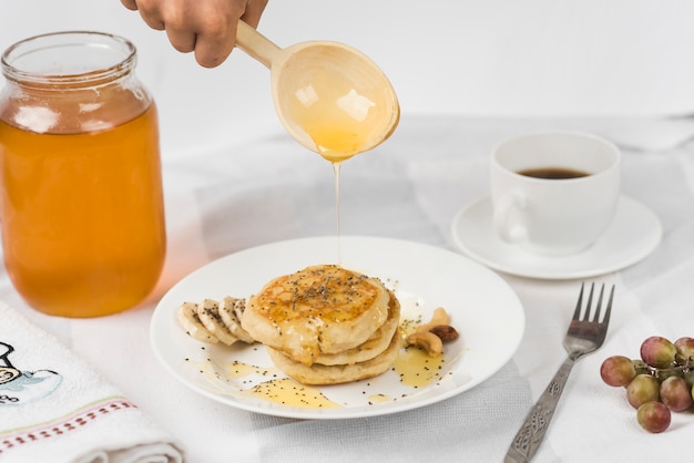 Close-up of hand pouring honey on pancake